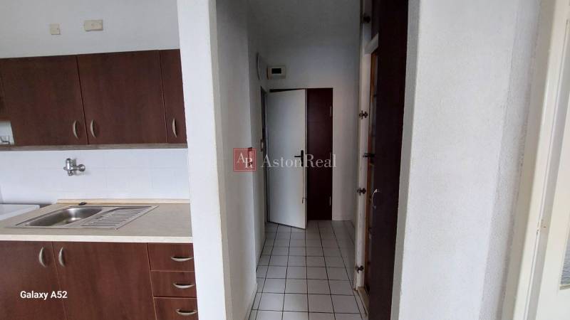 A kitchen with dark cabinets and white tiles in a studio apartment.