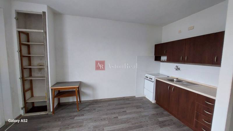 A kitchen in a studio apartment with dark cabinets and a wood-patterned floor.