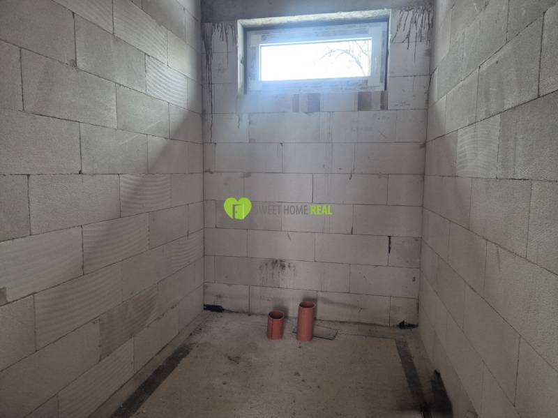 Unplastered walls, small window, and PVC pipes in a family house.