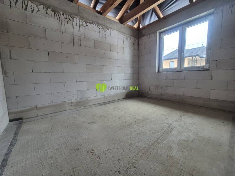 Concrete floor, unpainted bricks, and wooden beams in the interior of a family house.