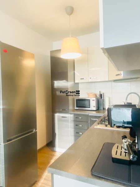A kitchen in a 2-room apartment with a cooktop, microwave, and a floor with a wooden decor.