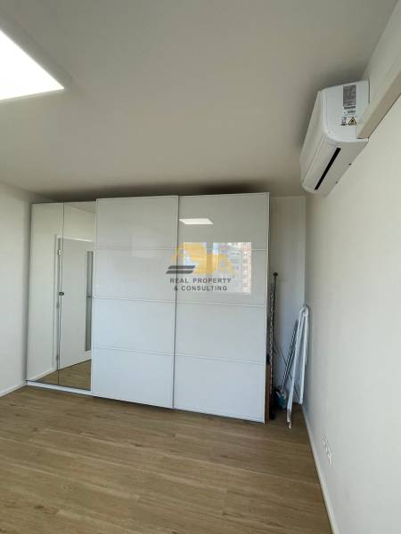 A studio apartment with a mirrored wardrobe and a wooden decor floor.