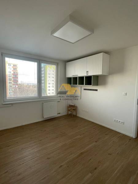 Interior of a one-room apartment with wood-patterned flooring and white walls, bright space.