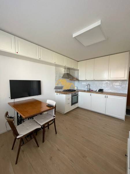 A kitchen in a studio apartment with a wood-patterned floor and a dining table.