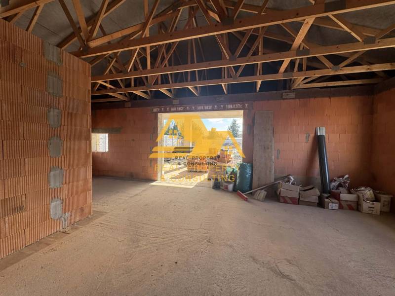 Unfinished interior of a family house with exposed wooden ceiling beams and raw bricks.
