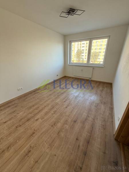 A room in a 2-room apartment with a wooden decor floor and a large window.