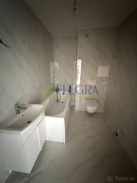 Bathroom in a 2-room apartment with a bathtub and a sink, tiled with light ceramics.