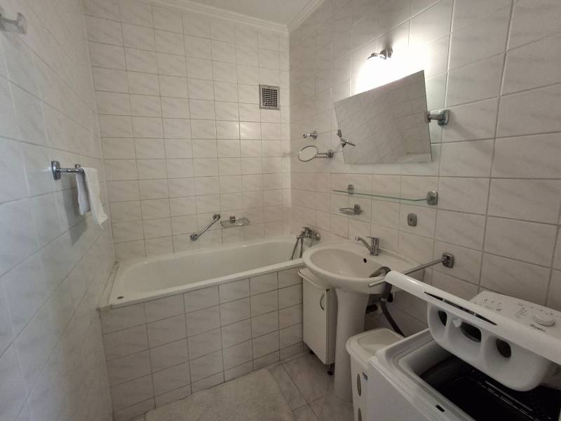 A bathroom with a bathtub and a washing machine in a 3-room apartment, tiled with light tiles.