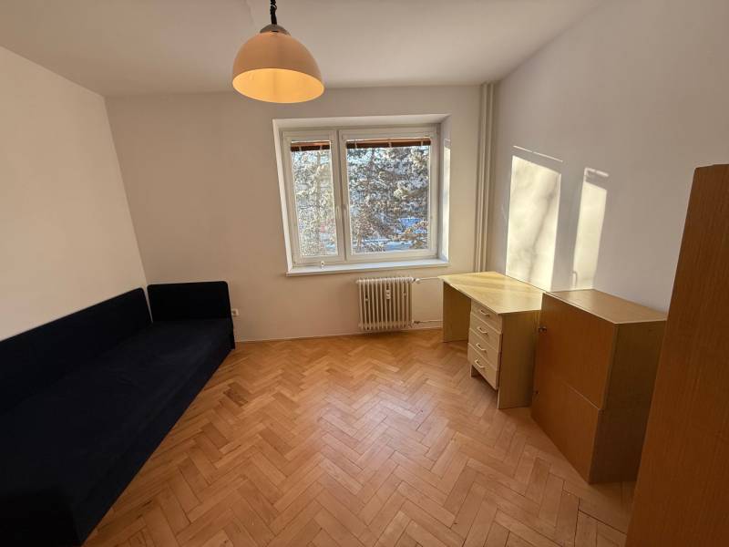 A room in a 3-room apartment with a wooden decor floor, a blue sofa, and a writing desk.