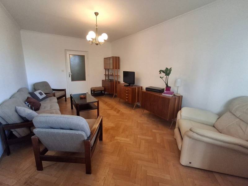 Living room of a 3-room apartment with a wooden decor floor, retro furniture, and comfortable armchairs.