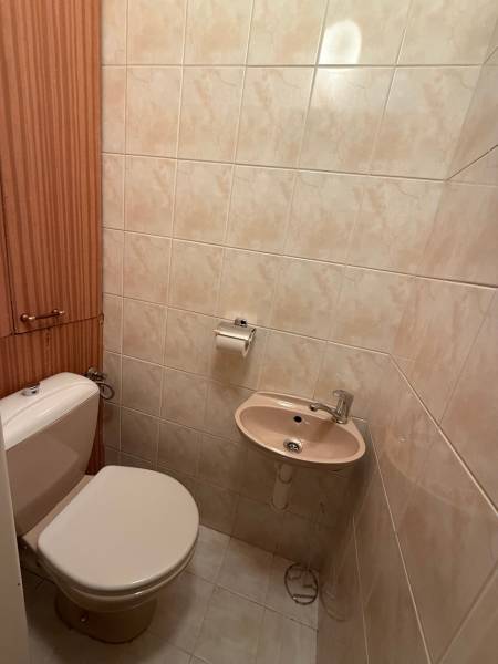 A bathroom with beige tiles, a toilet, and a small sink in a 3-room apartment.