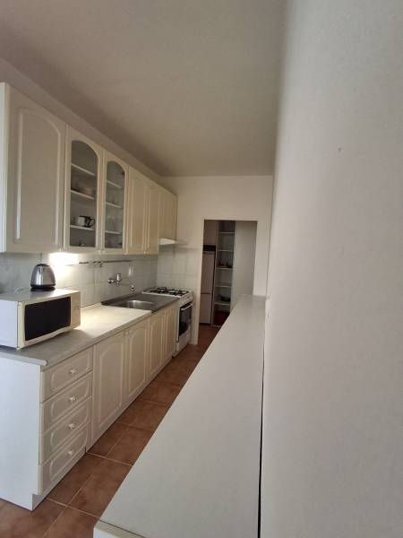 A kitchen with white cabinets and appliances in a 3-room apartment, floor with ceramic tiles.