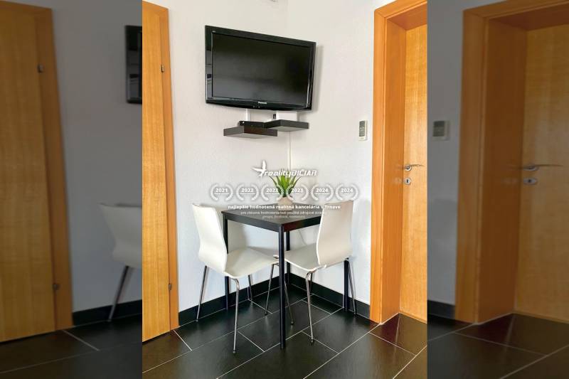 A dining room in a family house with a corner table, a TV on the wall, and black tiles.