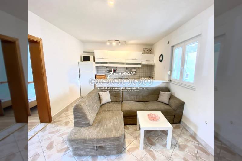 Living room in a family house with a sofa and a kitchenette, tiled floor.