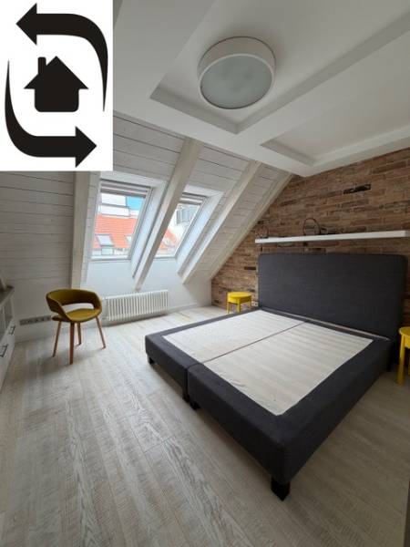 Bright attic bedroom with a double bed and wood-patterned flooring.