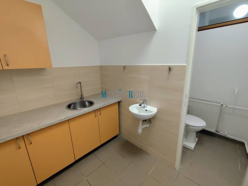 A sink, cabinets, and a toilet in commercial premises with light tiles on the wall.