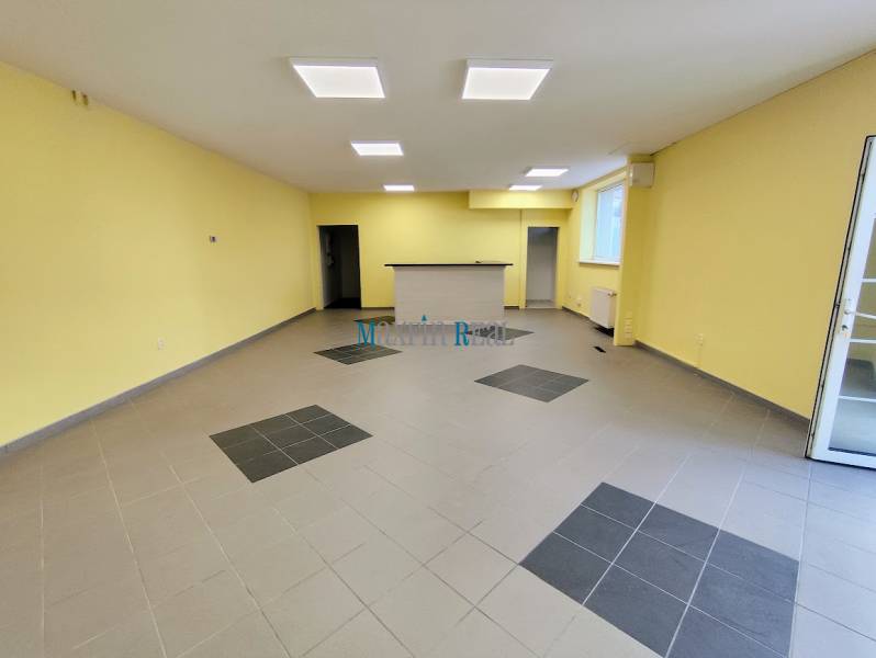 Interior of commercial spaces with tiled flooring and a reception area, illuminated by ceiling lights.