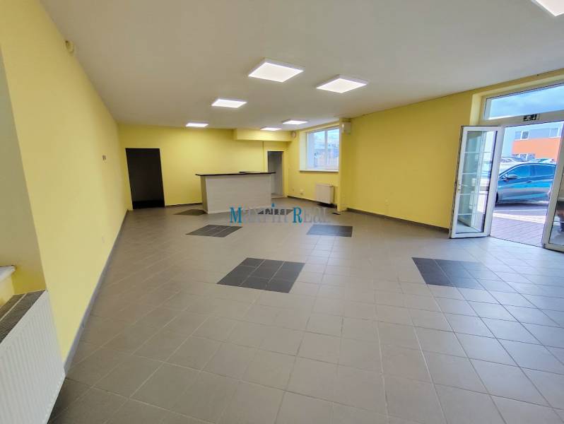 Commercial space with tiles and reception, yellow walls, large windows, entrance doors.