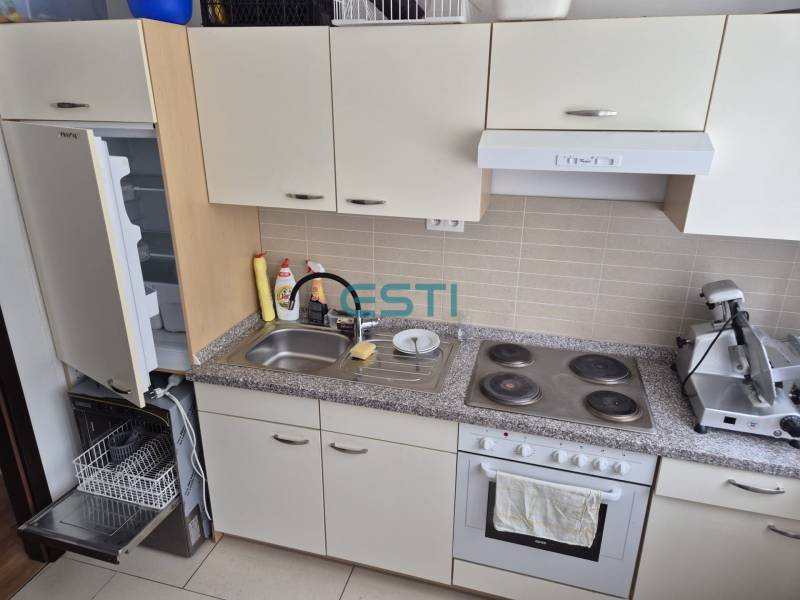 A kitchen unit in a one-room apartment with a dishwasher, stove, and open refrigerator.
