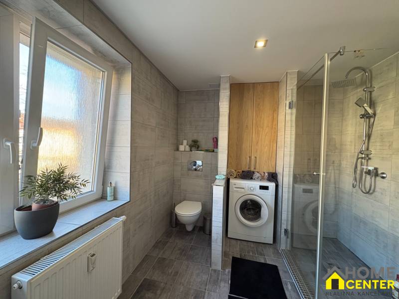 A bathroom in a 2-room apartment with a washing machine, shower, and window.