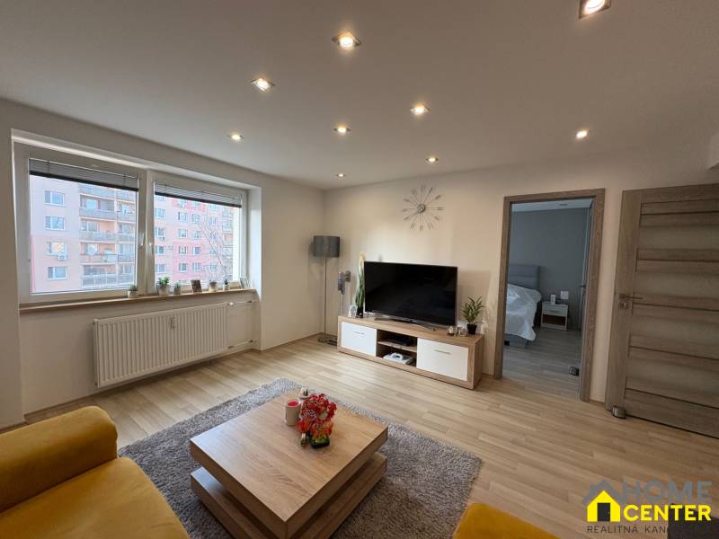 A bright living room in a two-room apartment with a wooden decor floor and a sofa.