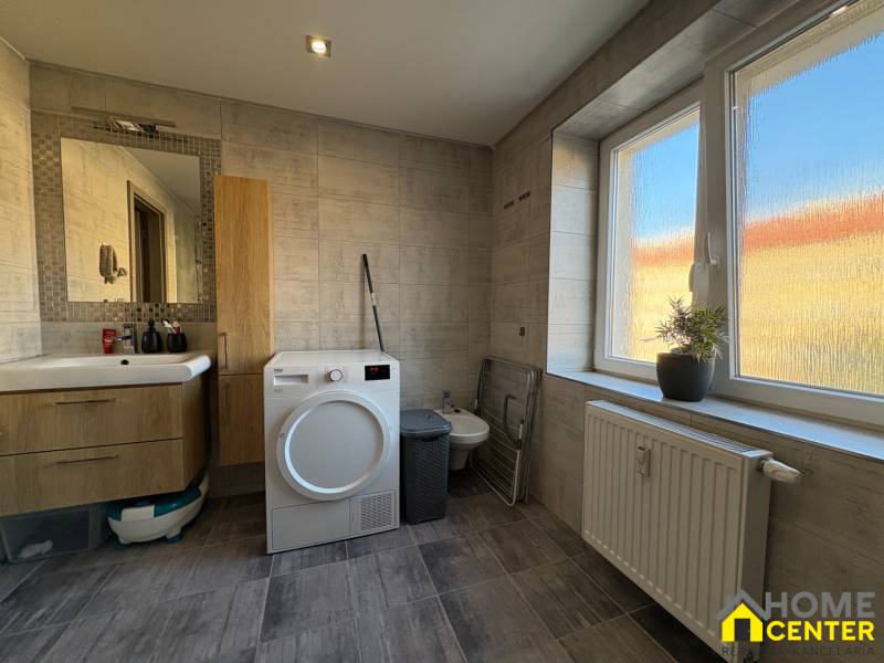 Bathroom in a 2-room apartment with a dryer, sink, and a large window with a plant.
