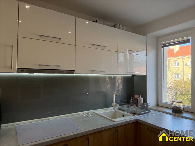 A kitchen in a 2-room apartment with white cabinets, an induction hob, and a light wood decor.