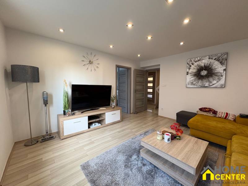 Living room in a two-room apartment with a wooden decor floor, TV, and yellow sofa.