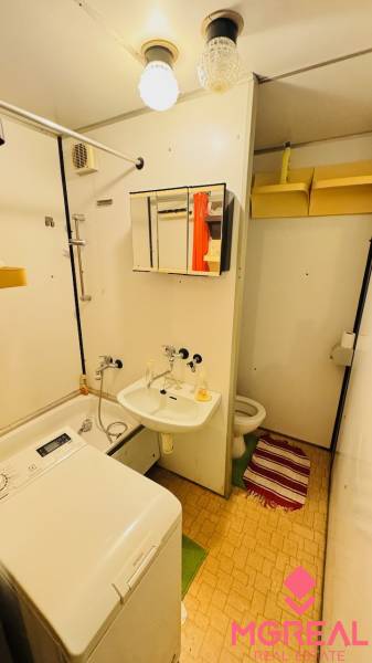 Bathroom with a sink, washing machine, and toilet in a 2-room apartment, simple storage solutions.