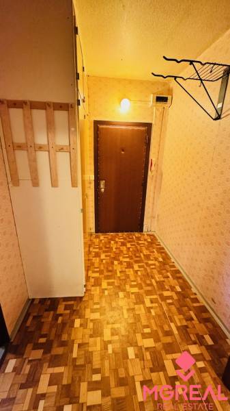 A hallway with a wooden decor floor and light wallpaper in a 2-room apartment.