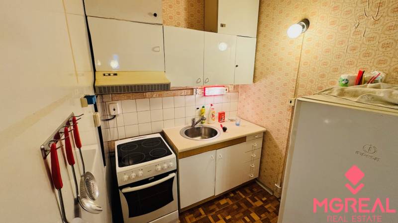 Kitchen in a 2-room apartment, white cabinets, stove, sink, floor with wood decor.