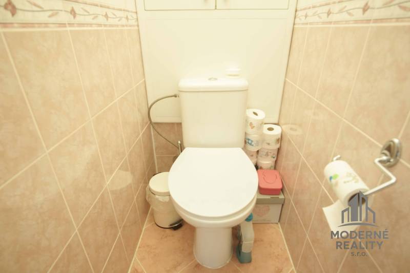 A toilet with beige tiles in a 3-room apartment with storage space for toilet paper.
