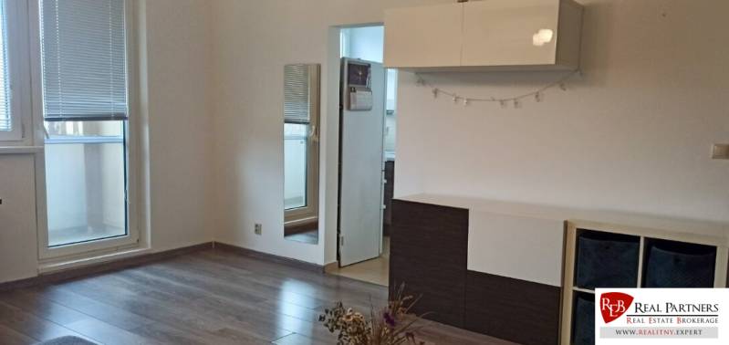 Living room in a two-room apartment with wood-patterned flooring, white furniture, and a mirror.