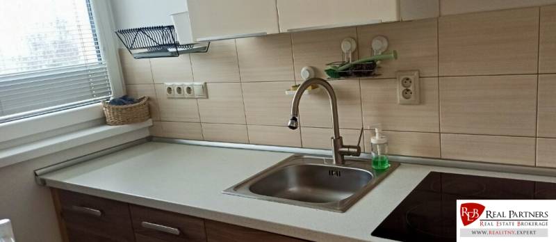 A kitchen in a 2-room apartment with a sink, a ceramic hob, and a basket by the window.