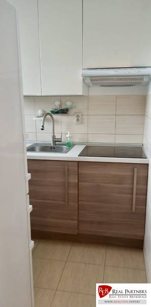 A kitchen with white cabinets and a stainless steel sink in a 2-room apartment.