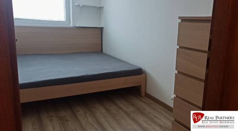 Bedroom in a 2-room apartment with a bed, wooden decor flooring, dresser, and shelves.