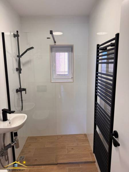 Bathroom in a 2-room apartment with wood-patterned flooring, a shower, and a window.