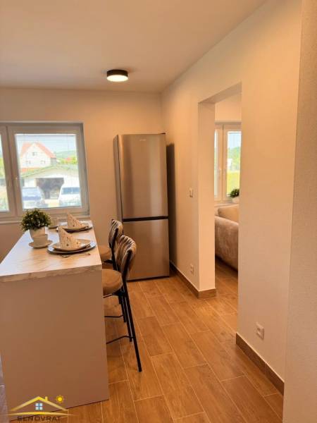 A kitchen in a 2-room apartment with a bar, wooden decor flooring, and a refrigerator.