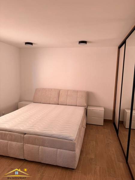 Bright bedroom of a two-room apartment with wood-patterned flooring and a comfortable bed.