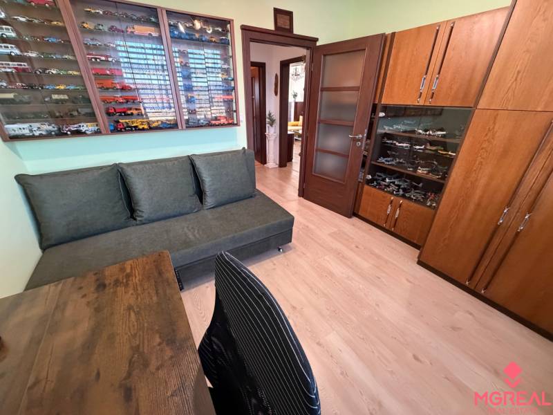 A room with a sofa, a display cabinet with models, and a floor with a wooden decor in a three-room apartment.