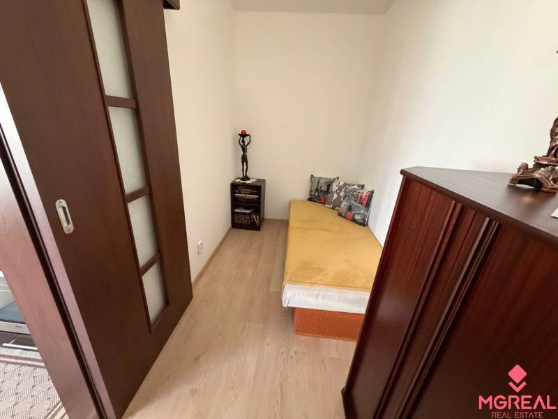 A room in a 3-room apartment with a bed, wooden decor flooring, dark furniture.