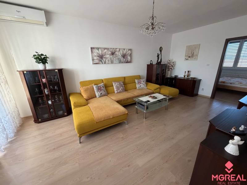 Living room with wood-patterned flooring, a yellow sofa, and a glass coffee table in a three-room apartment.