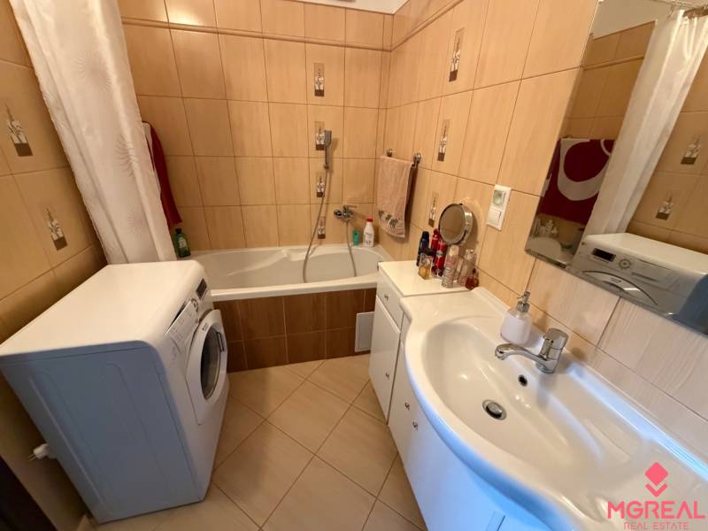 A bathroom with a shower and a bathtub in a 3-room apartment, with a washing machine and a sink.