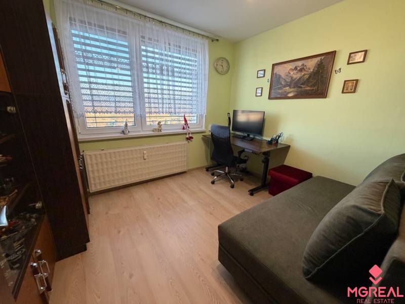A room with a wooden decor floor in a 3-room apartment, equipped with a sofa and a desk.