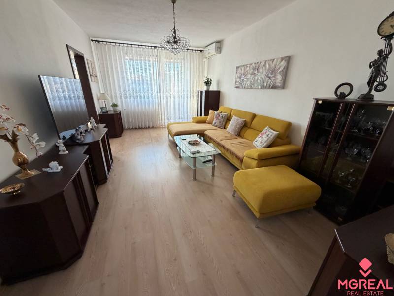 Living room with wood-patterned flooring in a three-room apartment with a yellow sofa.