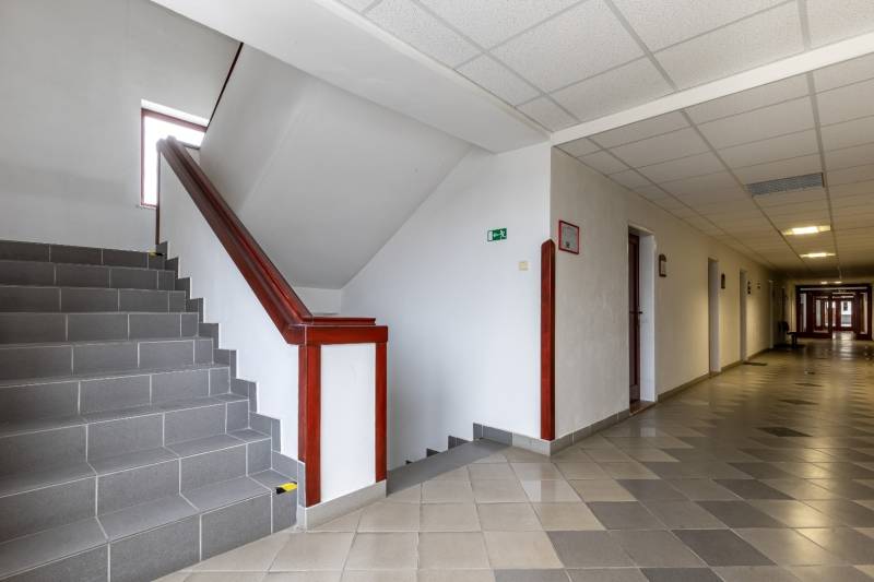 A corridor with tiles and a staircase in offices, ceiling lighting.