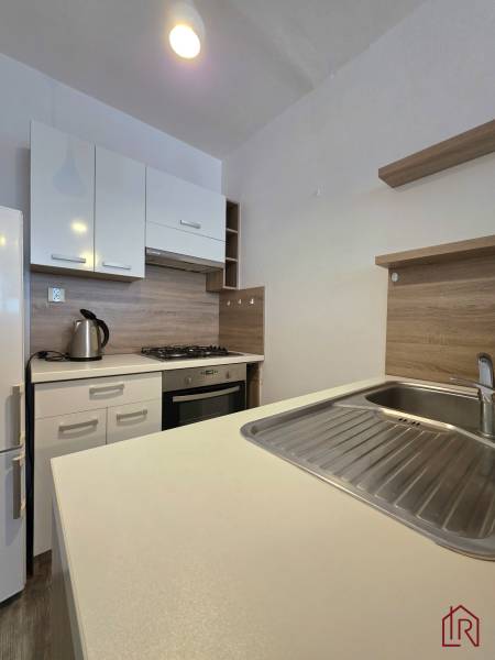 A kitchen in a 2-room apartment with a cooktop, a gas oven, and a floor with a wooden decor.