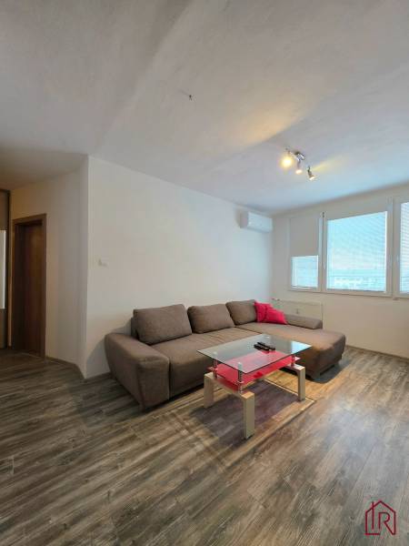 Living room with a brown sofa, glass table, wooden decor flooring in a 2-room apartment.