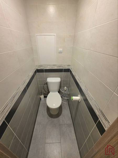 A toilet in a 2-room apartment with ceramic tile walls and flooring.