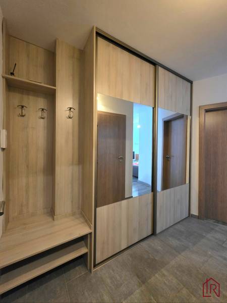 A wardrobe with a mirror and hangers in the hallway of a two-room apartment with a wooden decor floor.